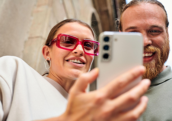 Zwei Personen schauen lachend aufs Smartphone, Selfie oder Social Media im urbanen Umfeld