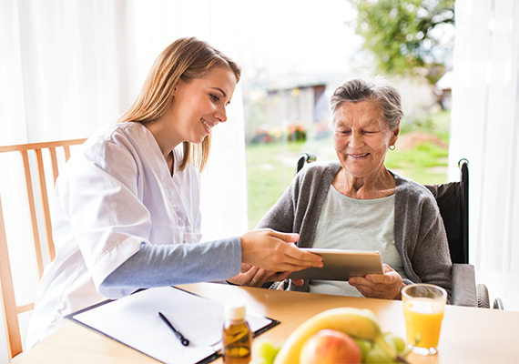 Pflegerin unterstützt Seniorin mit Tablet, digitale Gesundheitsberatung zu Hause