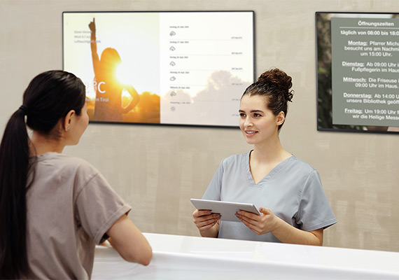 Rezeptionistin mit Tablet im Gespräch mit Patientin, digitale Anmeldung im Gesundheitszentrum