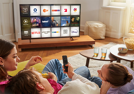 Drei Personen entspannen gemeinsam auf dem Sofa und schauen Magenta TV mit Streaming-Apps wie Netflix, Prime Video und Disney Plus