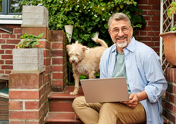 Schlechter Empfang war gestern Älterer Mann surft mit Laptop im Garten, Hund an seiner Seite – stabiles WLAN für Zuhause genießen.
