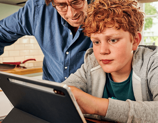 Vater und Sohn sitzen an einem Tisch aund schauen gespannt auf ein Tablet Vater und Sohn sitzen an einem Tisch aund schauen gespannt auf ein Tablet