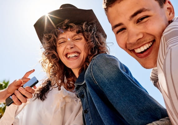 Zwei junge Menschen lachen gemeinsam bei Sonnenschein, Smartphone in der Hand, echte Freude im Moment
